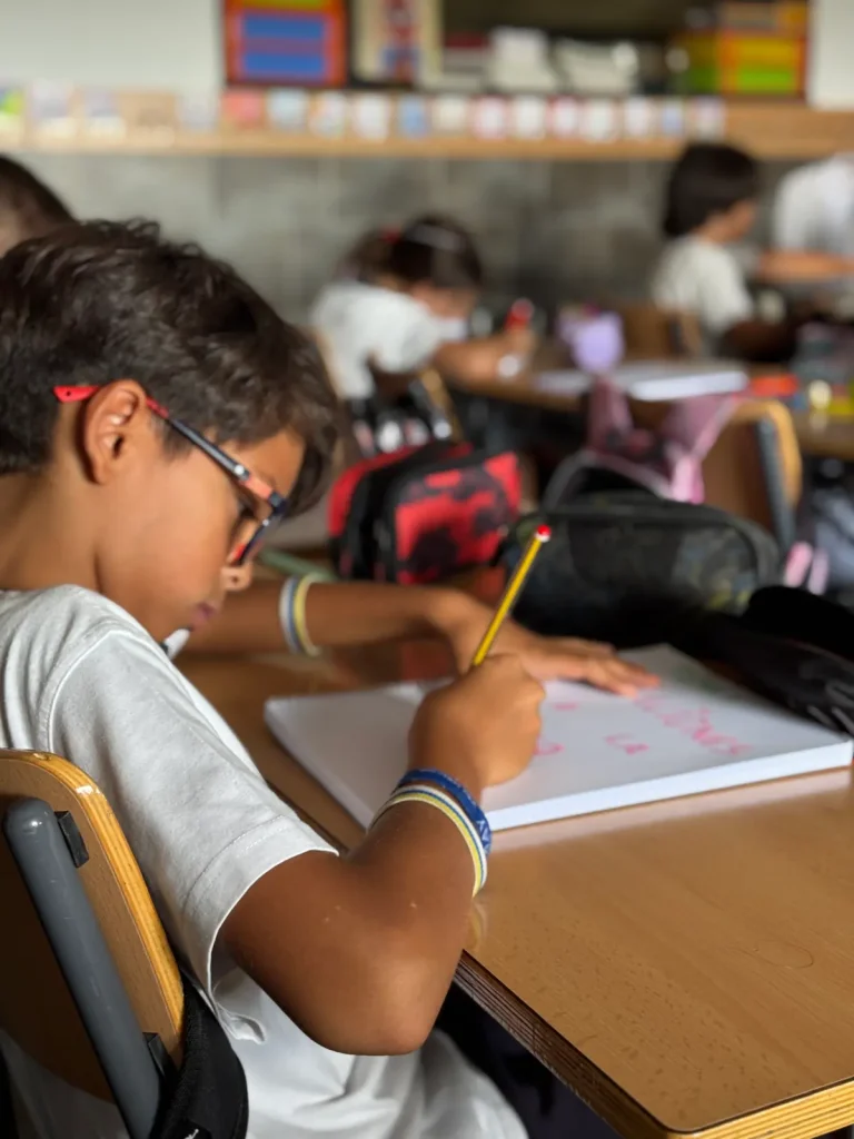 Alumno con gafas concentrado escribiendo con lápiz en su cuaderno