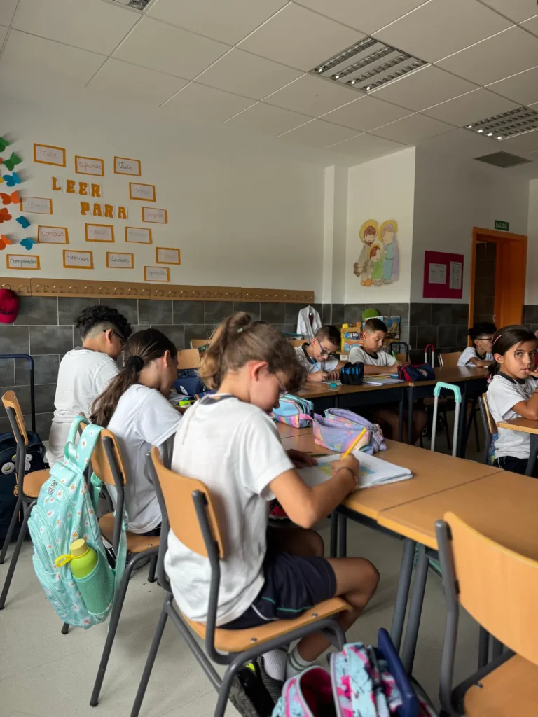 Vista general de un aula con los alumnos en sus pupitres y un mural de lectura en la pared