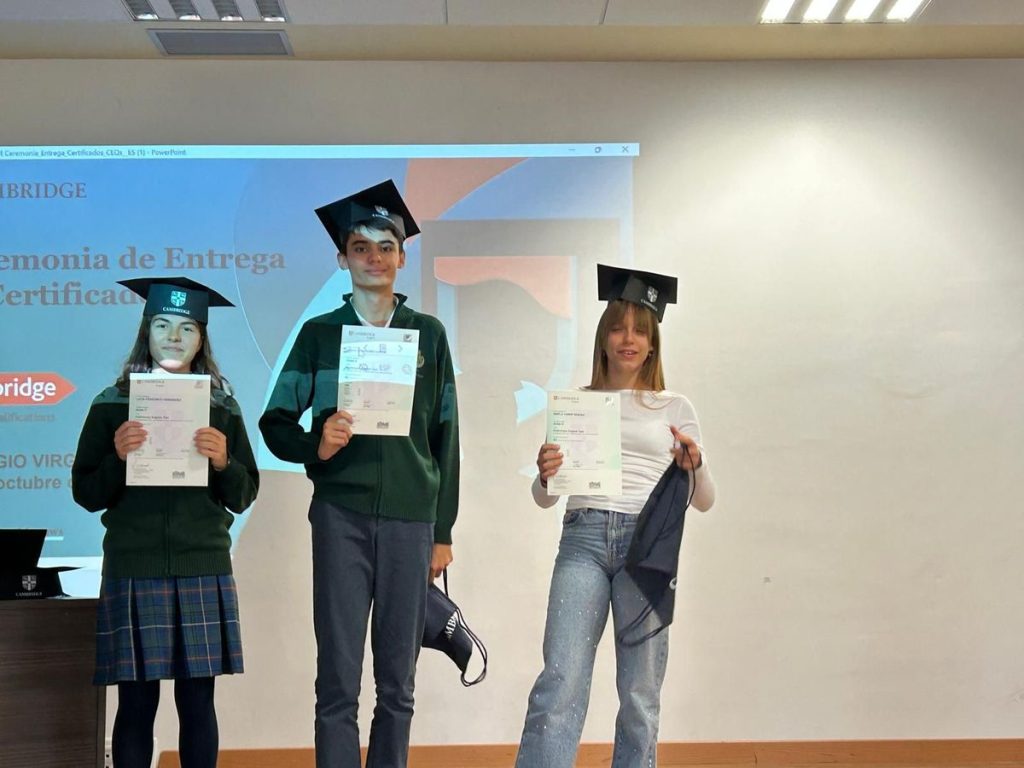 Alumnos con birrete mostrando sus certificados de Cambridge en el escenario