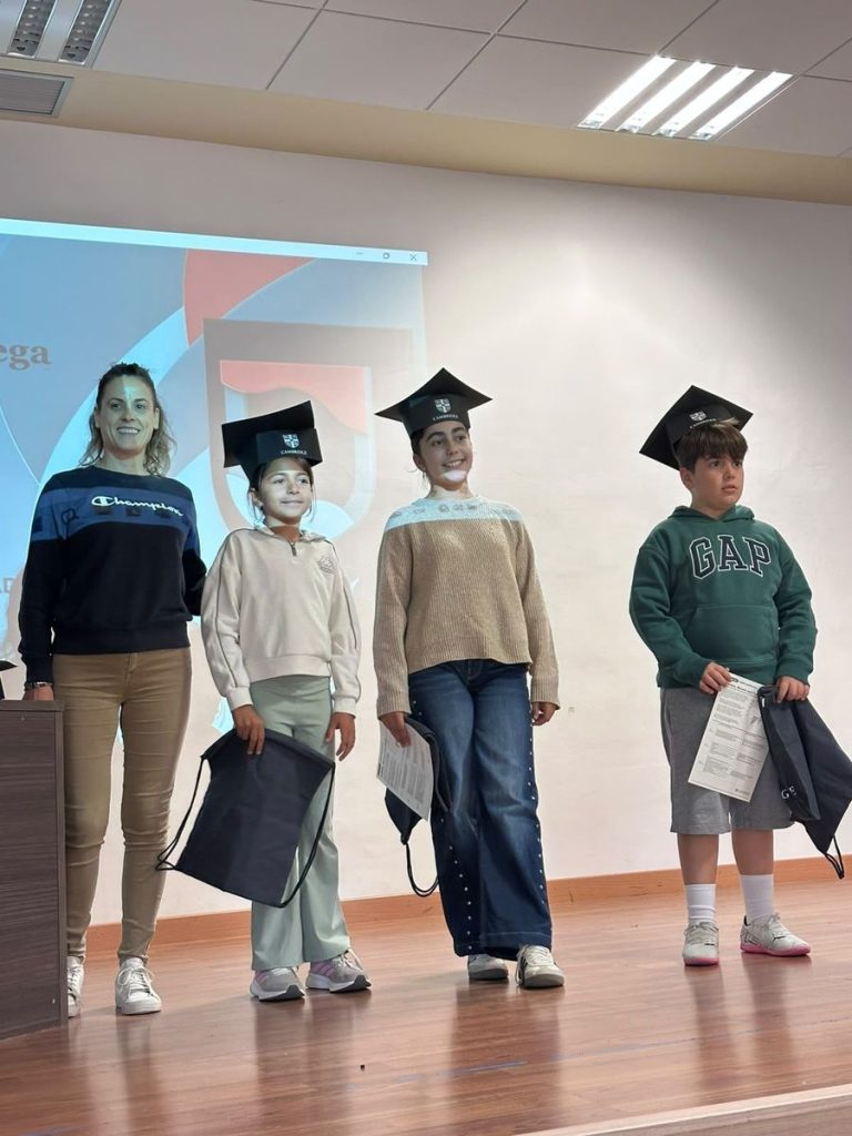Alumnos de Primaria con birrete y su certificado de Cambridge junto a su profesora