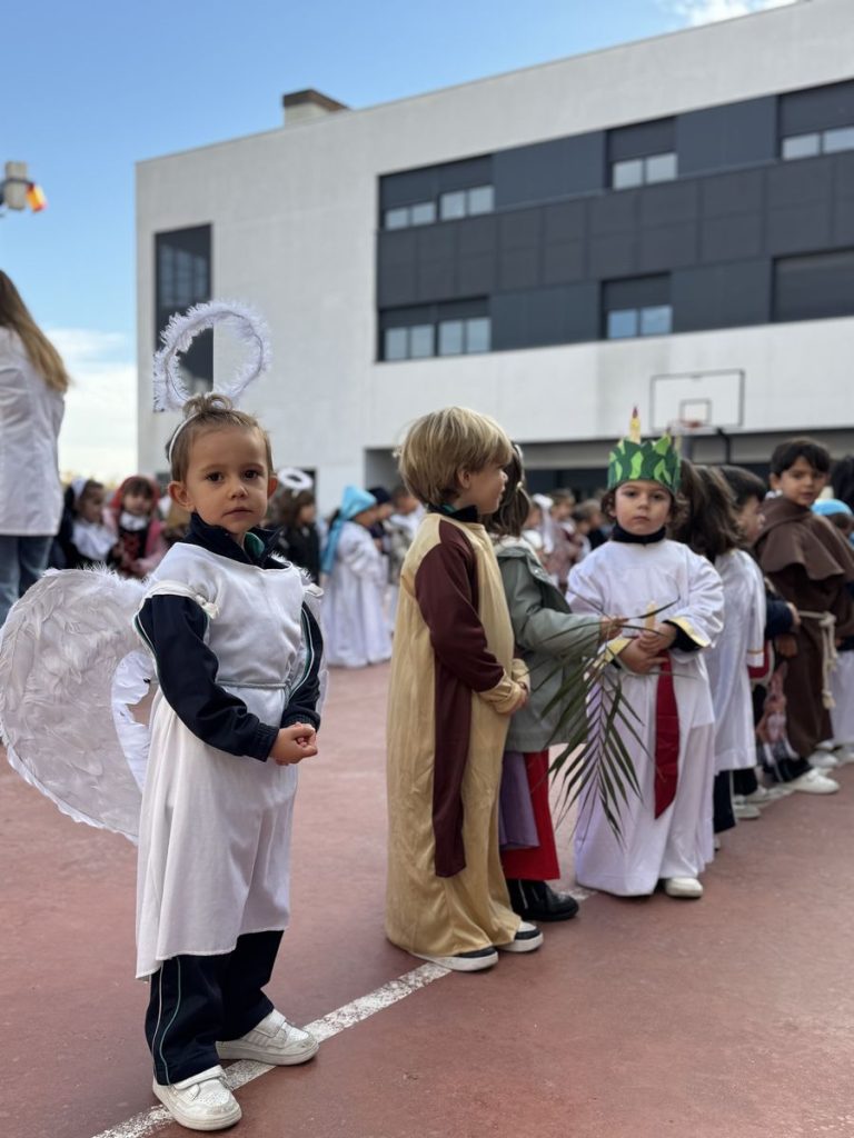 Alumnos de Infantil en fila disfrazados de santos y ángeles en el patio
