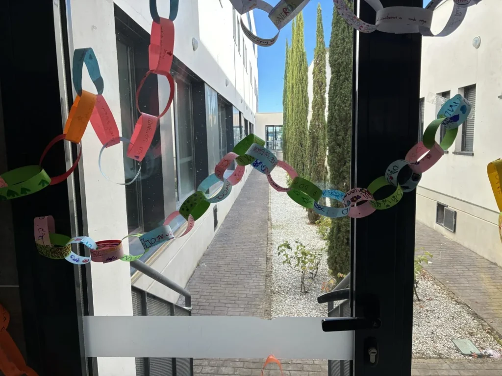 Cadena de eslabones de papel de colores con mensajes escritos a mano colgada en una puerta acristalada del colegio