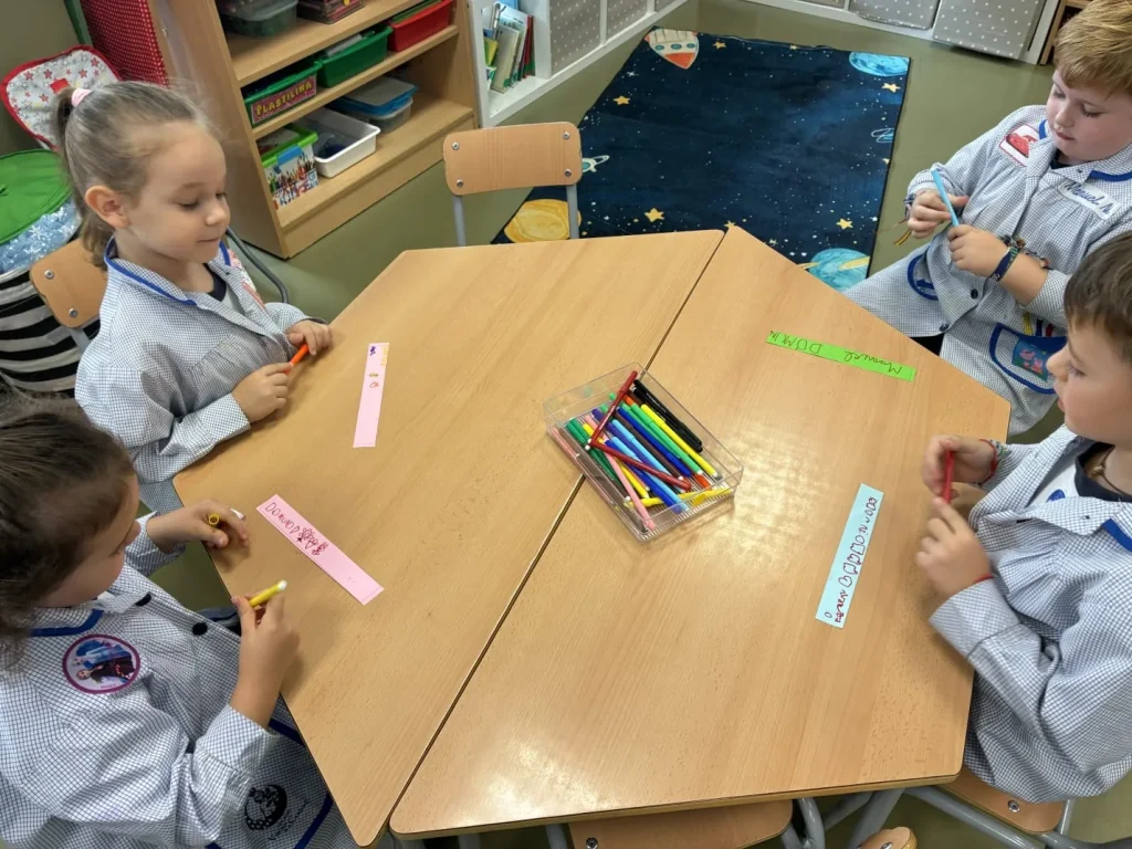 Alumnos alrededor de una mesa escribiendo y decorando tiras de papel de colores para la cadena del DOMUND